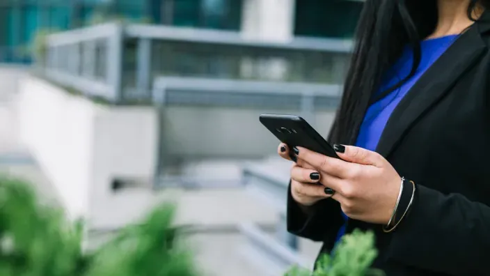 Profesional usando su smartphone frente a una oficina moderna.
