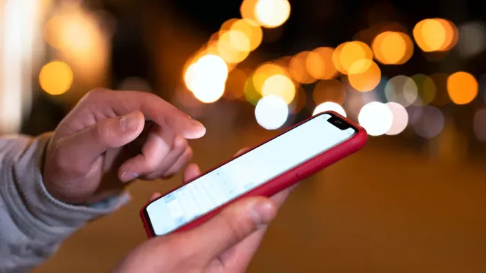 Persona usando un teléfono móvil por la noche con luces desenfocadas de fondo
