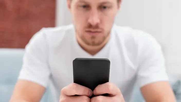 Hombre preocupado usando su smartphone ante un posible mensaje de fraude telefónico o estafa.