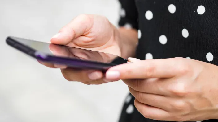 Primer plano de manos de mujer con vestido de lunares utilizando un smartphone negro.