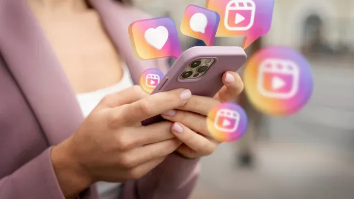 Manos sosteniendo móvil con iconos de redes sociales en pantalla.