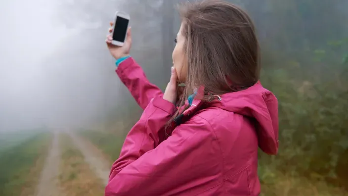Mujer buscando señal en su smartphone en un entorno con niebla para representar la conectividad móvil en zonas remotas.