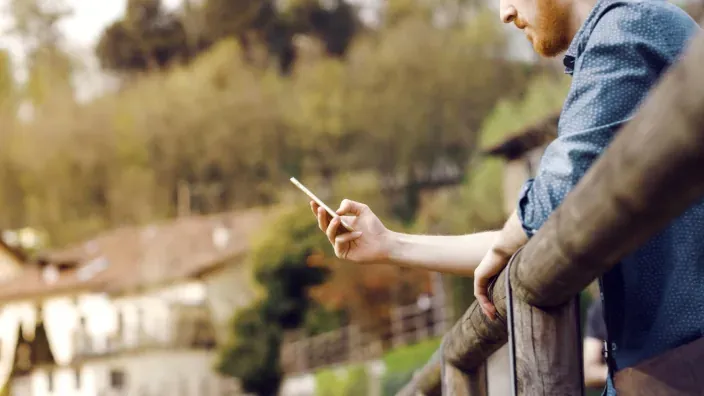 Hombre usando smartphone conectado a internet satelital en balcón con vistas a zona rural.