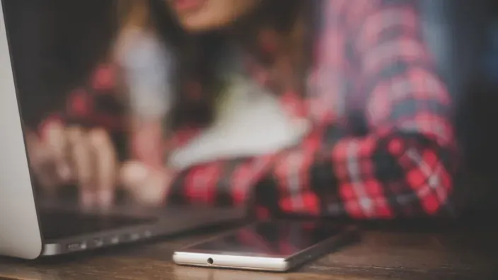 Mujer usando un portátil y un móvil para descargar apps de IPTV desde foros y enlaces externos.