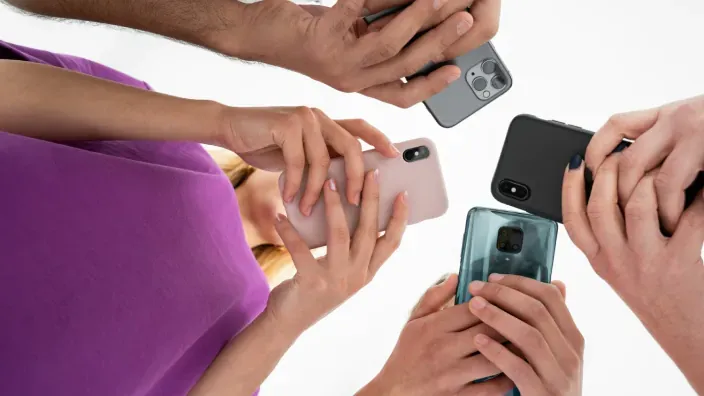 Grupo de personas sosteniendo y comparando diferentes modelos de teléfonos móviles en círculo.