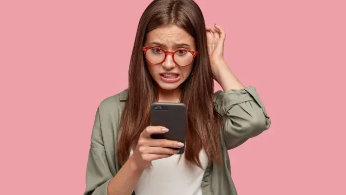 Mujer confundida mirando su teléfono móvil ante un posible problema de conectividad.
