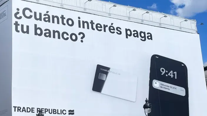 Valla publicitaria de Trade Republic con el mensaje “¿Cuánto interés paga tu banco?” junto a una tarjeta y un smartphone.