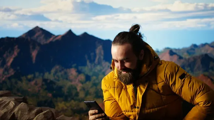 Hombre haciendo senderismo en la montaña, conectado a internet con su móvil.