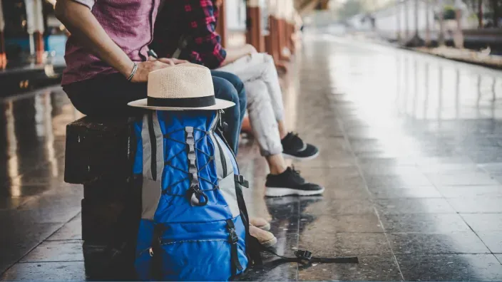 Viajeros sentados en una estación de tren con una mochila de viaje mientras esperan su salida