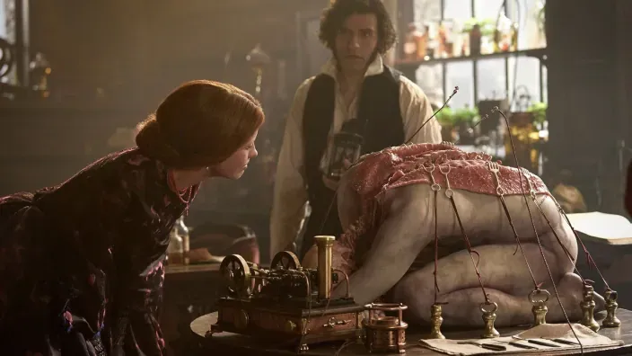 Una mujer y un hombre observan un cuerpo grotesco conectado a una máquina, en una escena de la película Frankestein