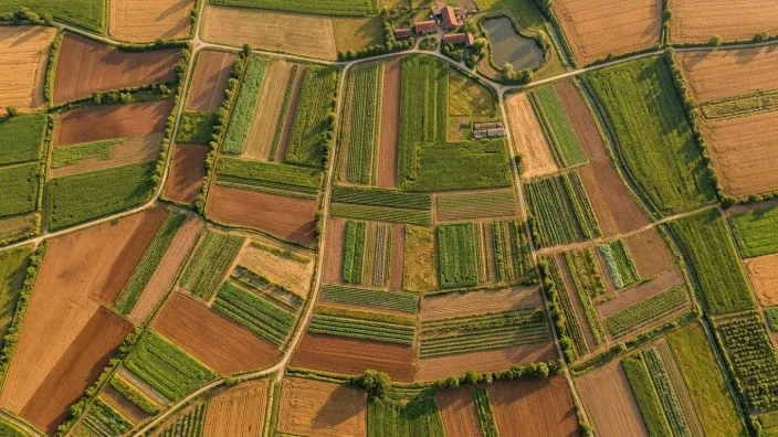 Vista aérea de campos agrícolas con parcelas de cultivos variados y una granja al fondo