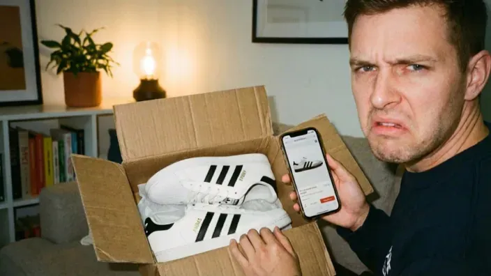 Hombre molesto mostrando zapatillas Adidas falsas recibidas por compra online.