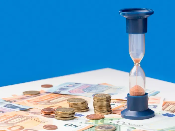 Reloj de arena sobre billetes y monedas de euro para representar la rentabilidad y el tiempo de los depósitos bancarios.
