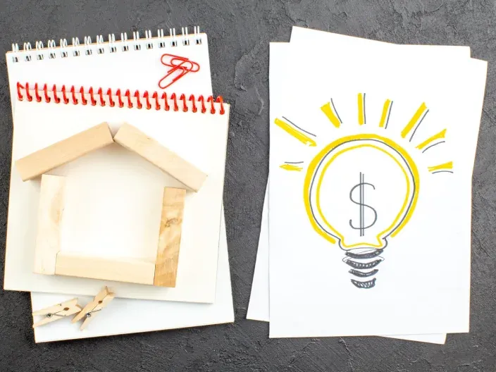 Concepto de ahorro en el consumo de luz con maqueta de casa en madera y dibujo de bombilla con dólar.