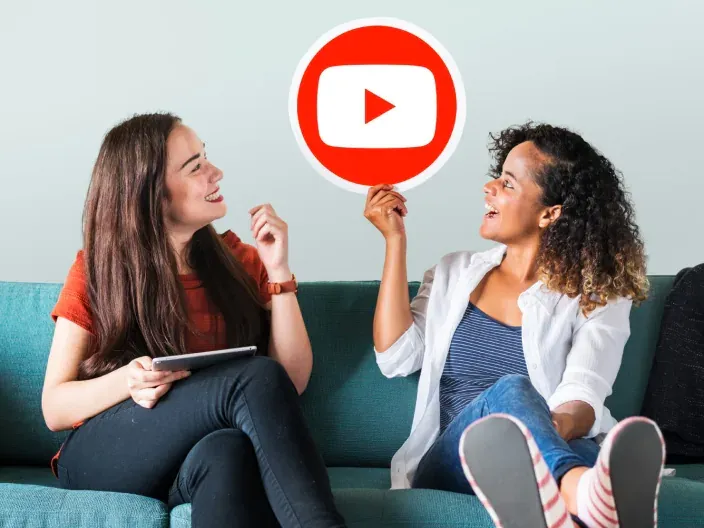 Mujeres con el logo de YouTube en un sofá para representar el consumo de contenido en streaming.