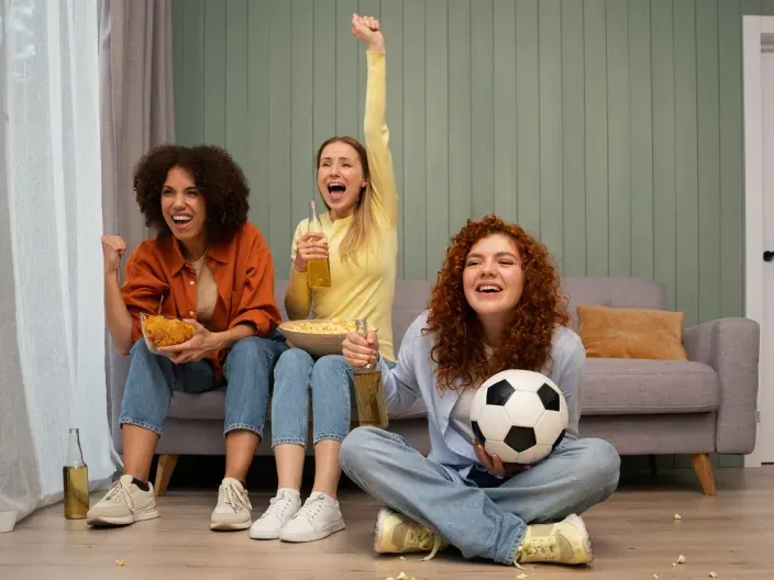 Grupo de amigas celebrando un gol mientras ven un partido de fútbol en casa. 
