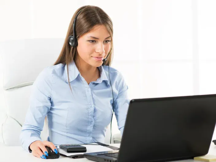 Agente de atención al cliente con auriculares trabajando frente a un ordenador portátil en una oficina.