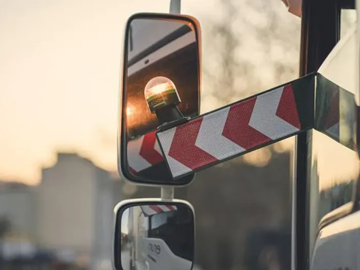 Espejo retrovisor de un camión con una luz de emergencia y bandas reflectantes para mejorar la seguridad en carretera.