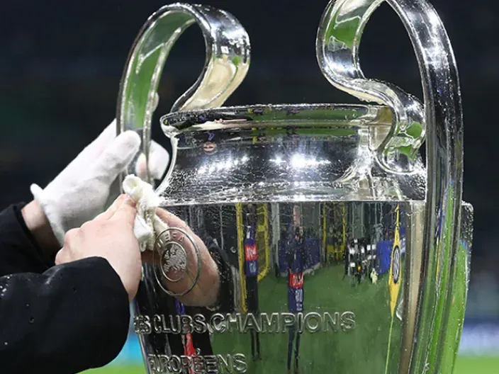 Primer plano del trofeo de la UEFA Champions League siendo pulido por manos con guantes blancos.