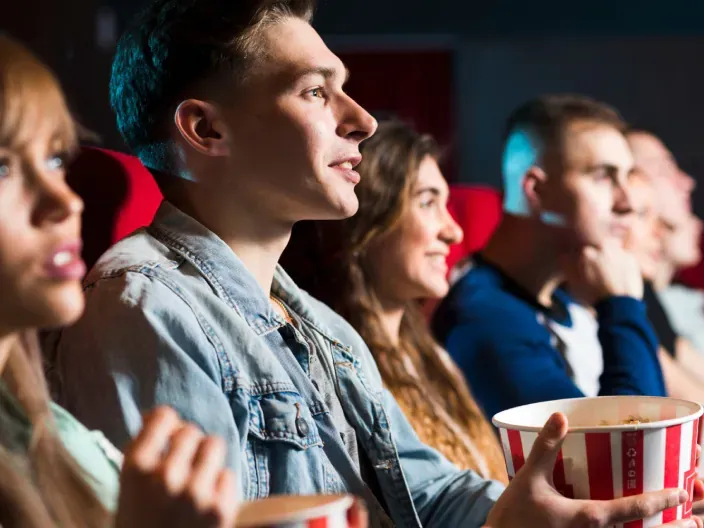 Espectadores en una sala de cine viendo una película con un cubo de palomitas en un ambiente de ocio.