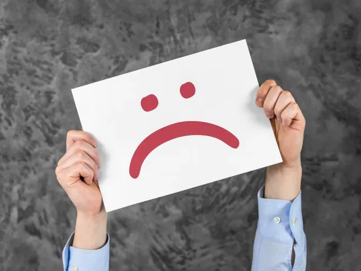 Cliente sosteniendo hoja de papel con dibujo de cara triste por mal servicio o queja.