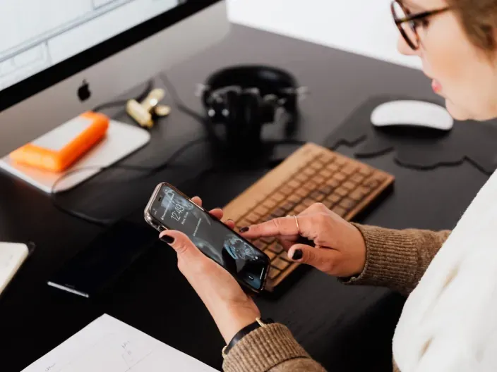 Usuario utilizando un smartphone en un escritorio de oficina con ordenador para gestiones de conectividad digital.
