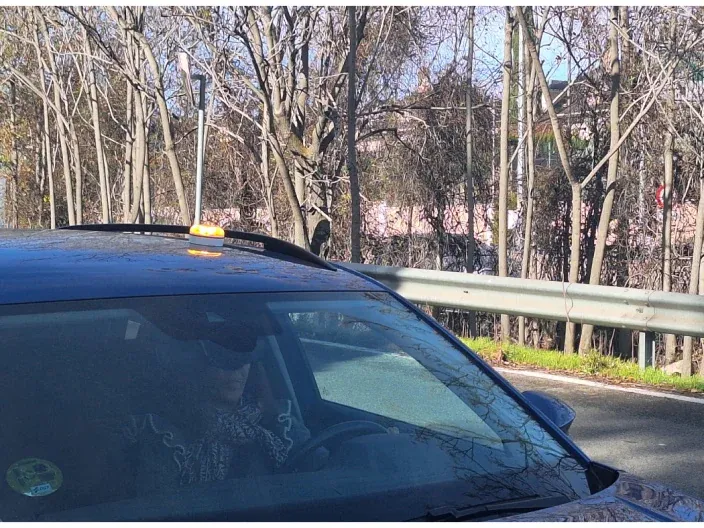 Coche azul oscuro averiado con baliza V16 de señalización en el techo en el arcén de la carretera.