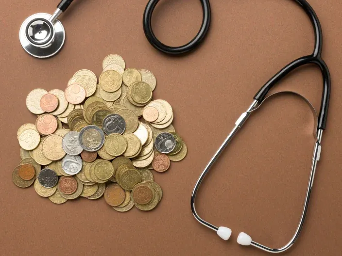 Concepto del coste de la sanidad: un estetoscopio y monedas. El precio de un seguro de salud y los gastos médicos.