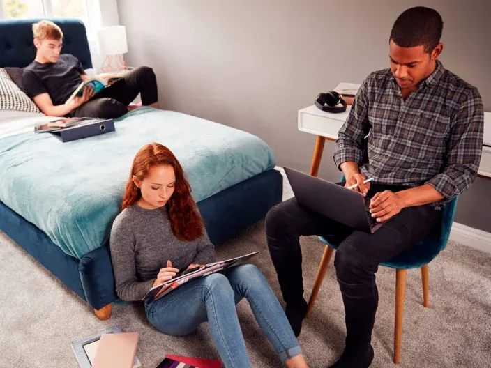 Tres estudiantes universitarios estudiando en su habitación con un portátil, reflejando el uso de internet en casa.
