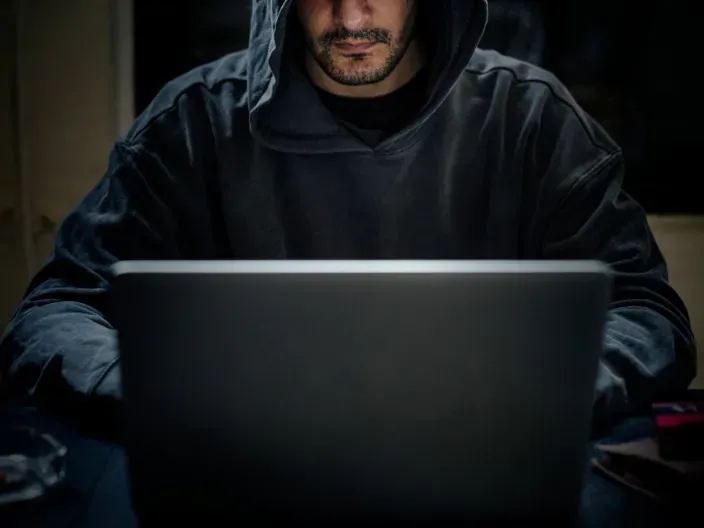 Hacker con sudadera oscura frente a un portátil a oscuras como concepto de ciberdelincuencia y falta de seguridad.