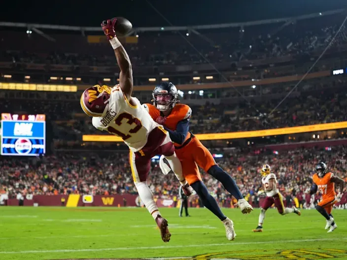 Jugador de los Washington Commanders atrapando el balón mientras un defensor de los Denver Broncos intenta placarlo