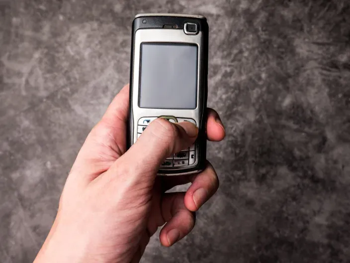 Mano sujetando un teléfono móvil antiguo con teclado físico, símbolo de la tecnología obsoleta y redes 3G.