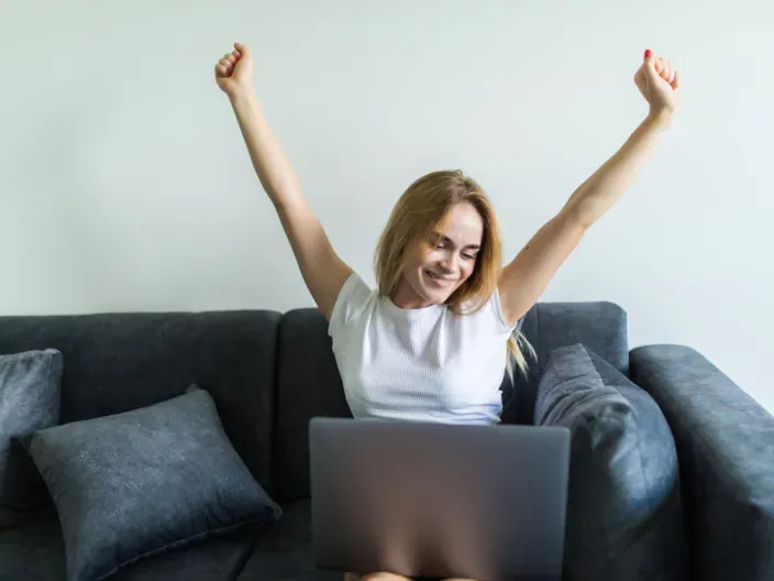 Mujer celebrando buena conexión a internet con su portátil en el sofá.
