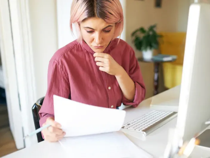 Mujer joven con gesto de preocupación revisando sus facturas.