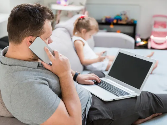 Padre teletrabajando en el sofá junto a su hija. El reto de la conciliación familiar y la flexibilidad laboral.