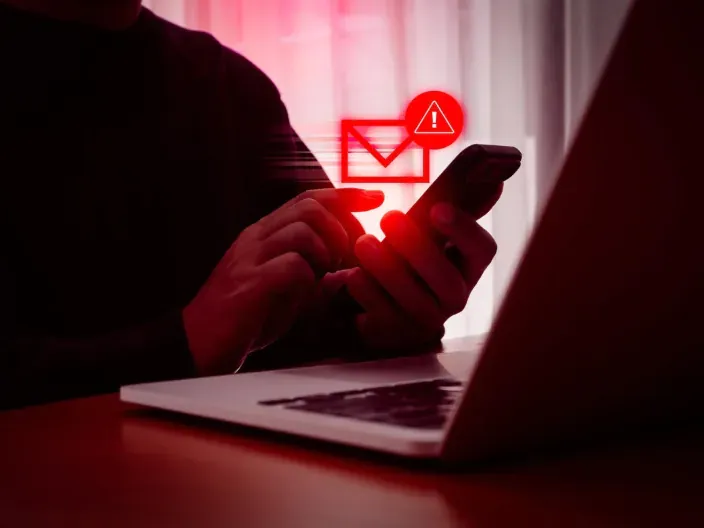 Alerta de phishing y ciberseguridad: persona recibiendo un mensaje malicioso en su smartphone frente a un portátil.