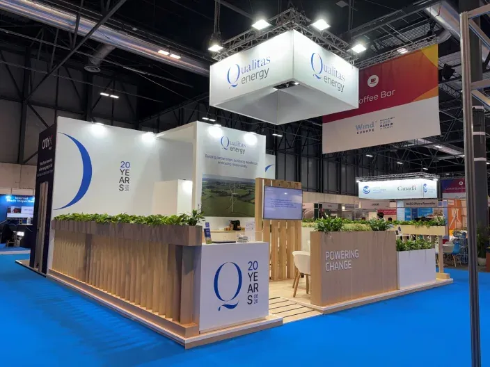 Stand de Qualitas Energy en una feria con mostradores, plantas y carteles corporativos