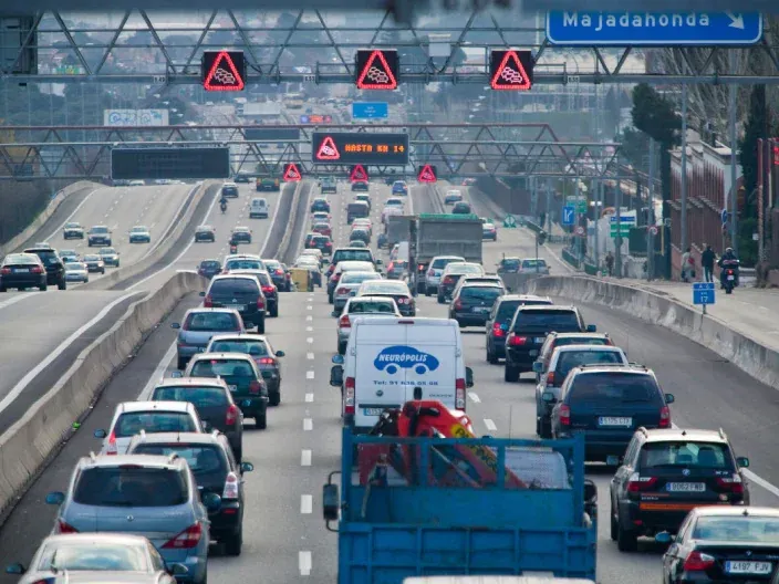 Tráfico denso con numerosos coches circulando y señales luminosas de advertencia en una autovía cerca de Madrid.