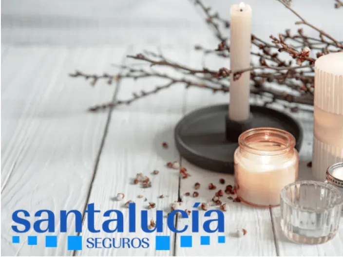 Vela encendida y elementos decorativos sobre una mesa de madera con el logotipo de Santalucía Seguros en la esquina.