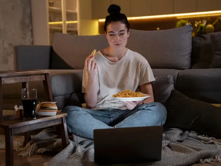 Joven cenando mientras ve una serie o película en su portátil.
