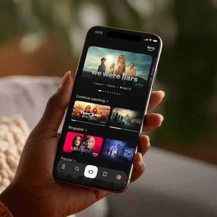 Usuario viendo la serie Landman en su smartphone con la aplicación Fire TV desde el sofá de su casa en streaming.