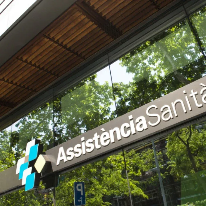 Entrada de una oficina de Assistència Sanitària en Barcelona con el logo visible en la fachada acristalada.