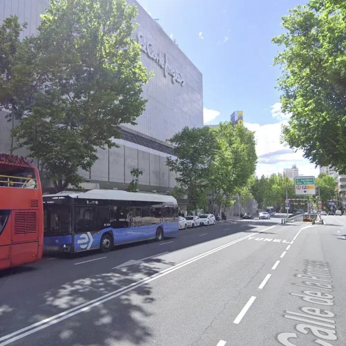 Fachada de El Corte Inglés en la calle de la Princesa en Madrid con un autobús de la EMT y otro turístico.