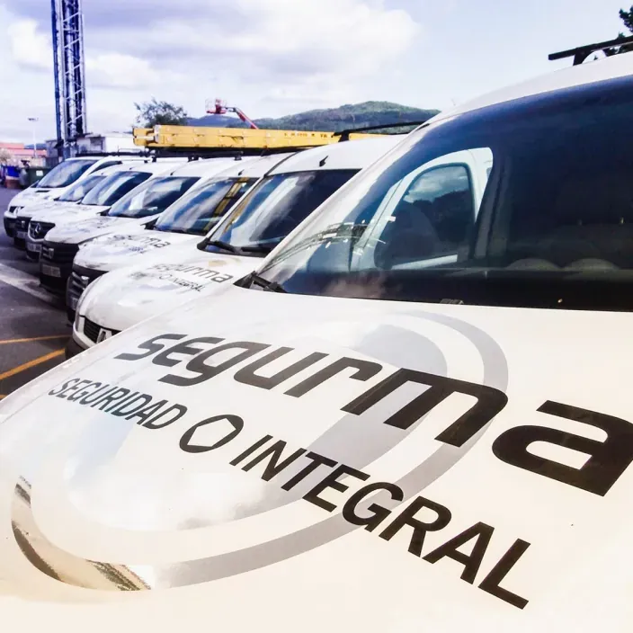 Fila de furgonetas de Segurma Seguridad Integral aparcadas en un recinto exterior