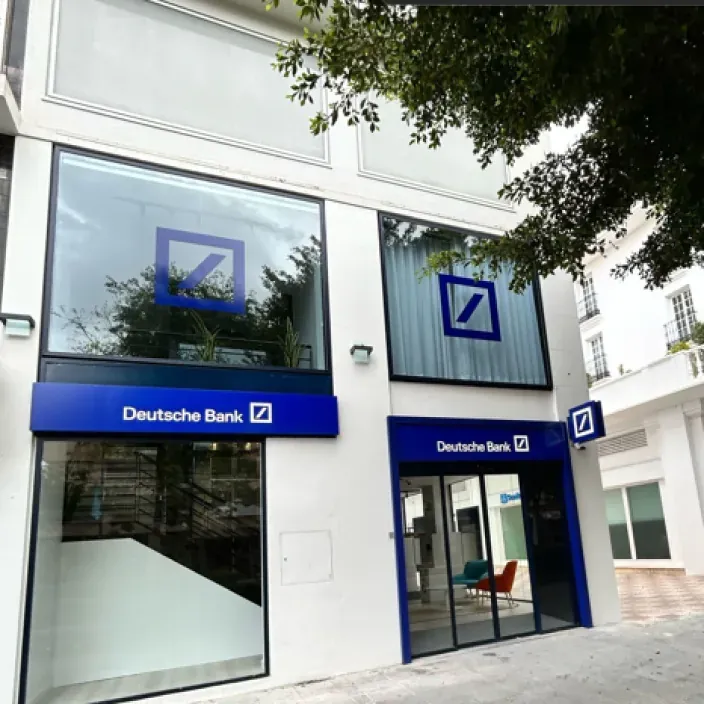 Fachada moderna de una oficina de Deutsche Bank con cristaleras y el logotipo azul visible en el exterior