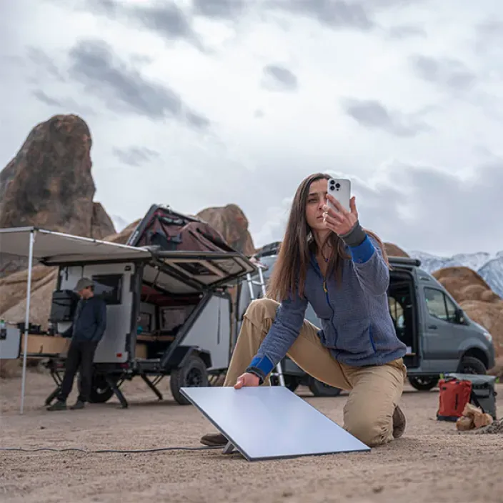Mujer orientando antena Starlink con smartphone en un camping para obtener internet satelital portátil.