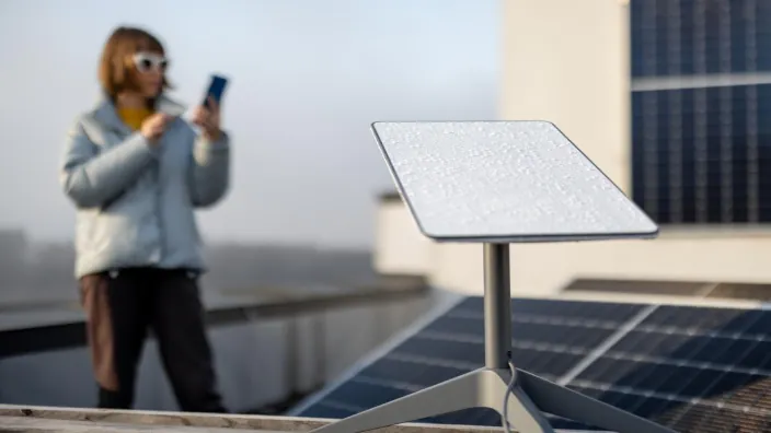 Antena satelital Starlink instalada en un tejado con paneles solares y una mujer usando su smartphone al fondo.