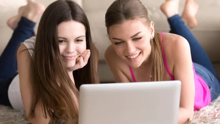 Dos amigas viendo juntas ofertas de fibra óptica en un portátil.