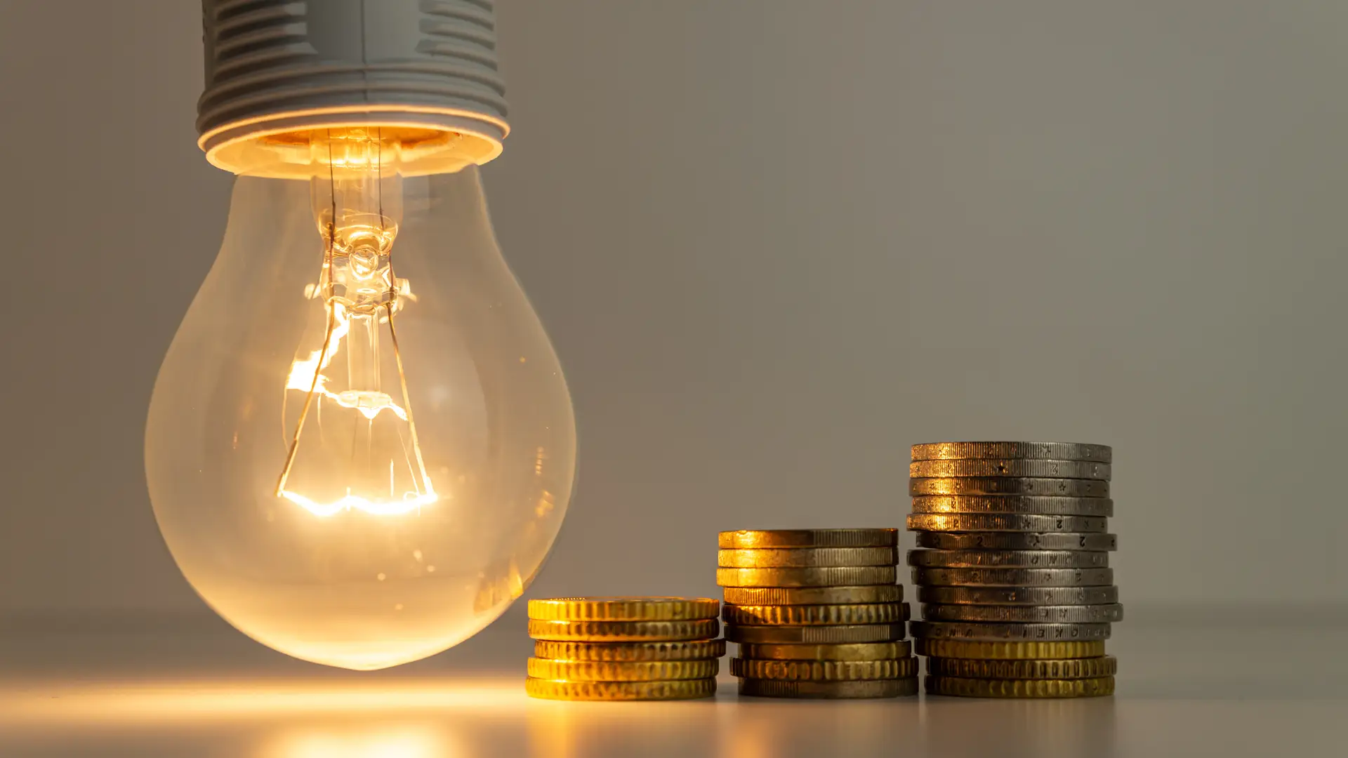 Unas torres de monedas junto a una bombilla para representar el precio de solar 360 Unas torres de monedas junto a una bombilla para representar el precio de solar 360