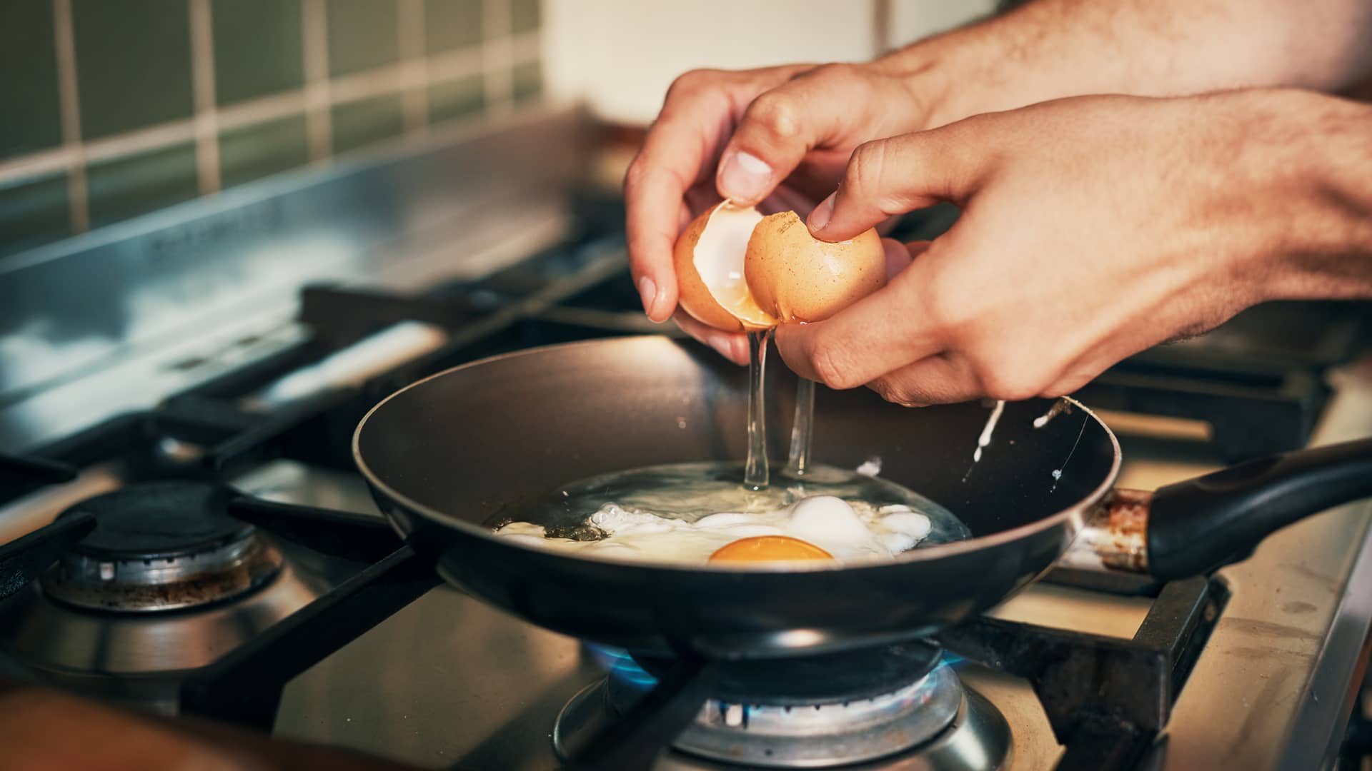 Hombre friendo huevo en cocina de gas natural